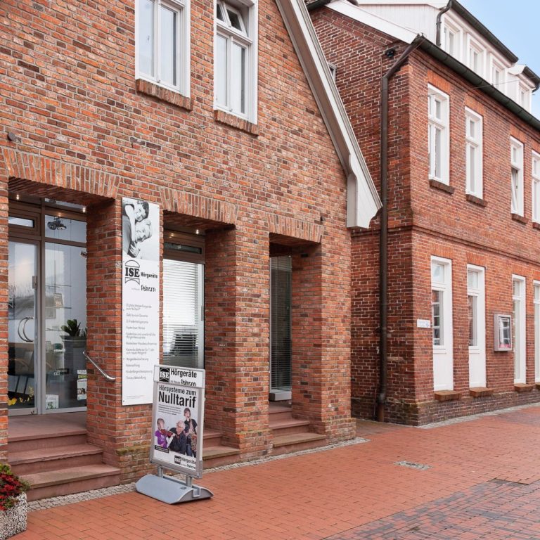 ISE Hörgeräte Filiale Wittmund Zweistöckiges, rotes Backsteingebäude mit Fenstern und Eingängen, moderne Fassade.