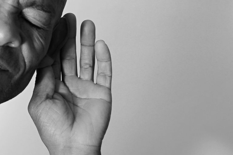 Tinnitus Ein naher Blick auf ein Gesicht, das zur Hand an das Ohr neigt, in schwarz-weiß.