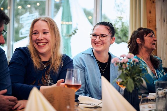 ISE Mitarbeiter feiern zusammen Lächelnde Personen an einem Tisch, mit Blumen und Getränken in einem gemütlichen Ambiente.