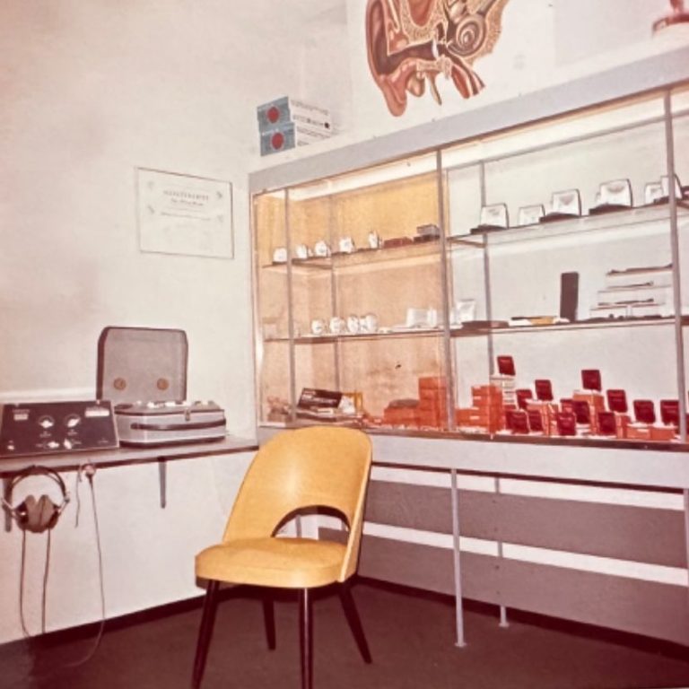 Alter Anpaßraum aus den 60er 70er Jahren Ein Raum mit einem gelben Stuhl, einem Regal mit Hörgeräten und einem Gerät zur Audiometrie.
