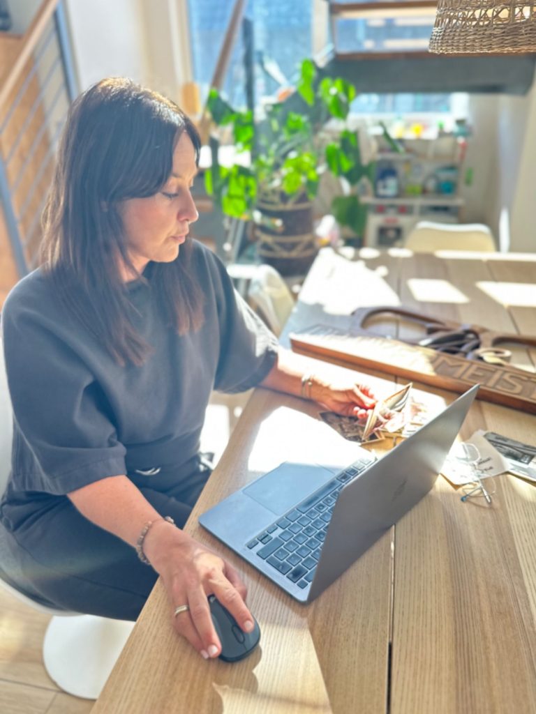 Janna Ise Frau arbeitet am Laptop an einem hellen Schreibtisch mit Pflanzen im Hintergrund.