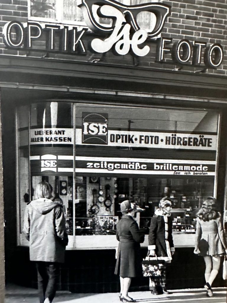 Altes Foto des ISE Optikgeschäftes Schaufenster des Optikgeschäfts ISE mit einer Gruppe von Passanten. Schwarzweißes Foto aus den 50er/60er Jahren