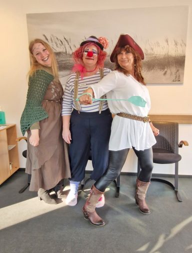 Helau Drei Personen in bunten Kostümen: eine Frau im Kleid, ein Clown und eine Piratin.